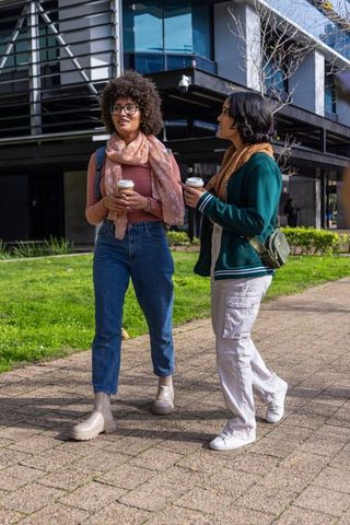 Campus coffee walk: friends walking and chatting while holding coffee on university path