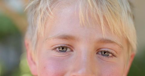 Closeup portrait of smiling blond boy gazing with light blue eyes and soft garden bokeh