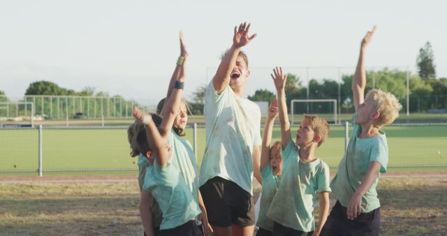 Young children enjoying physical activity on school field, raising hands in celebration and excitement. Perfect for educational content, sports and fitness promotions, community events marketing, and outdoor activity campaigns.