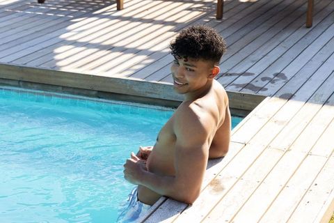 Smiling african man sitting on pool edge relaxing with turquoise water and sunlit deck