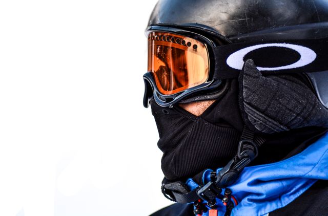 Close-up showing skier wearing black helmet and orange goggles, prepared for cold weather. Great for use in winter sports advertisements, skiing equipment promotions, or articles on outdoor activities.