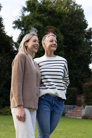 Women wearing festive merry christmas headbands smiling together in backyard garden