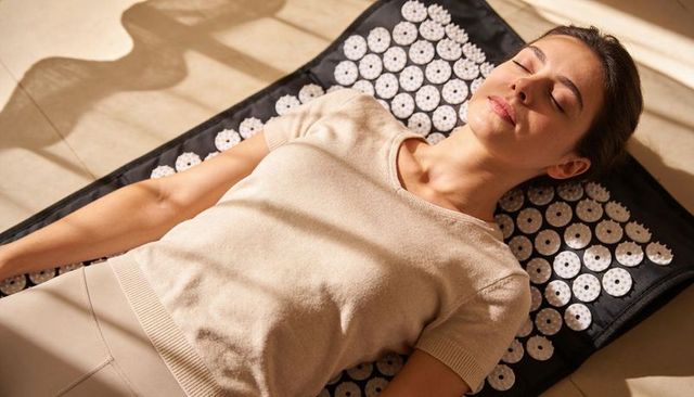 Young woman relaxing on acupressure mat in sunlit home for wellness and stress relief