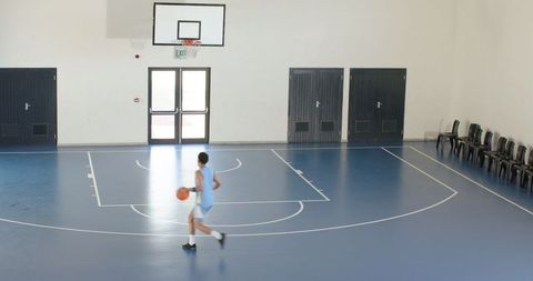 Athlete Dribbling Basketball on Indoor Court With Blue Flooring