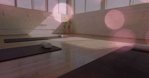 Sunlight casting soft bokeh over lined yoga mats with rolled towels in bright studio