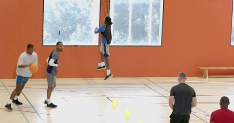 Basketball players jumping and dribbling during energetic indoor training drill with cones