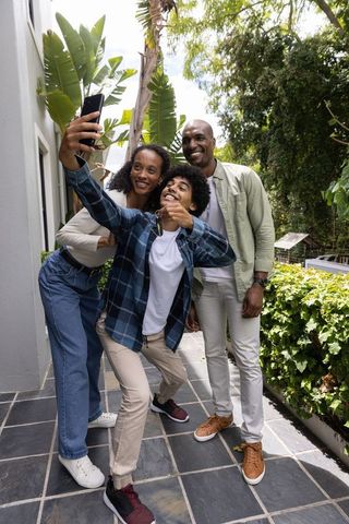 Smiling diverse family taking selfie on sunny patio with teenage son holding keys