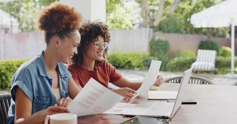 African american women collaborating on charts and laptop at backyard workspace