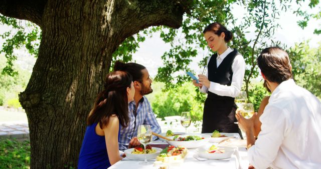 Friends Enjoying Outdoor Meal with Waitress Taking Order Under Tree - Download Free Stock Images Pikwizard.com