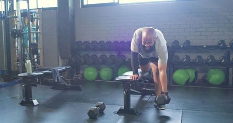 African american man performing one-arm dumbbell row on bench in gym, strength training