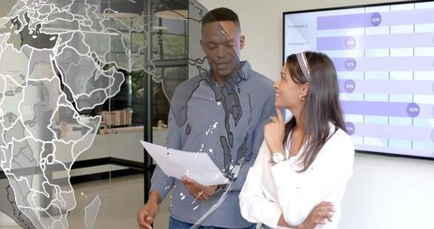 Young professionals collaborating over report by glass world map and analytics dashboard