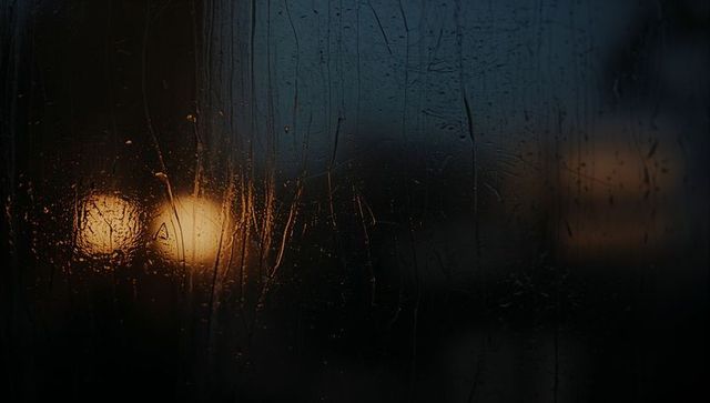 Rain-Smeared Glass Capturing Warm Bokeh Glow and Streaked Raindrops at Night