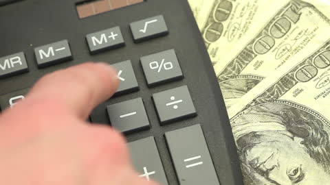 Close-up of Hand Using Calculator with Dollar Bills