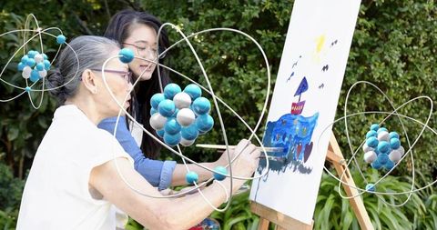 Intergenerational art: senior and adult woman painting outdoors with atom sculptures