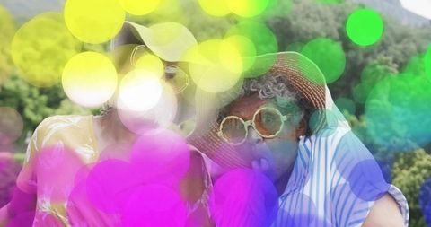 Senior women wearing sun hats and sunglasses enjoying colorful bokeh in sunny garden