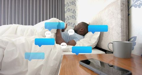 Man scrolling smartphone in bed with floating chat bubbles for messaging and relaxation