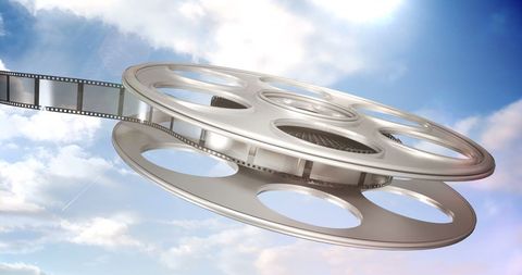 Classic Film Reel with Expanding Film Strip Against Cloudy Sky