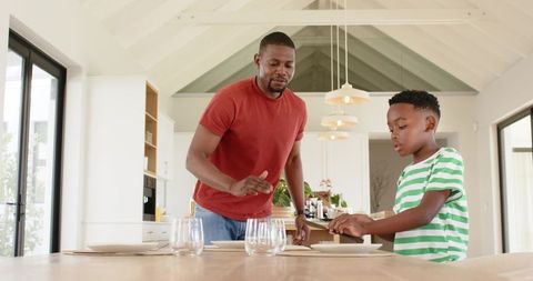African American Father and Son Arranging Tableware in Bright Modern Kitchen