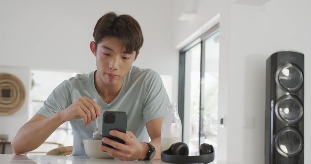 Asian boy using smartphone while having breakfast in living room at home. teenager lifestyle and living concept