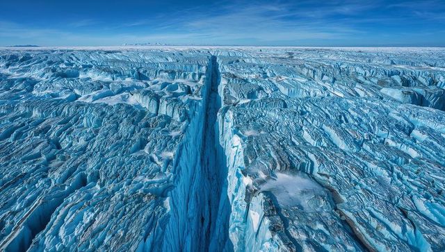Aerial surveying deep crevasse cutting across polar glacier with jagged seracs and melt ponds