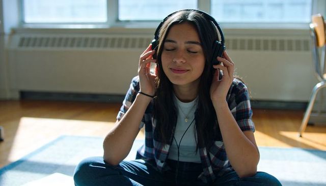 Young woman listening to music with headphones sitting on floor in sunlit living room