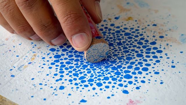 Hand pressing cork stamp creating dense blue dot pattern on paper for craft backgrounds