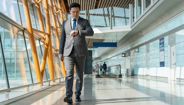 Asian businessman walking through modern airport terminal checking watch, business travel