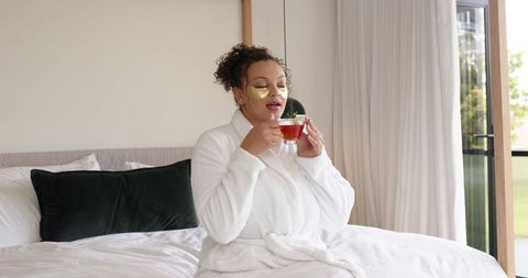 African american woman enjoying self-care, wearing gold under-eye patches and sipping tea