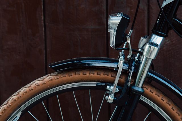 Detailed view of a bicycle's front wheel and headlight, captured against a wooden wall. Perfect for websites or articles about cycling, bike maintenance, outdoor activities, transportation, or environmentally friendly practices. Can be used in advertisements for bike accessories, cycling gear, or fitness equipment.
