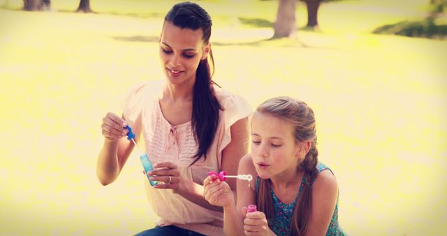 A young Caucasian woman and a girl are enjoying a sunny day outdoors blowing bubbles, with copy space. Their shared activity reflects a moment of leisure and bonding, between a mother and daughter.