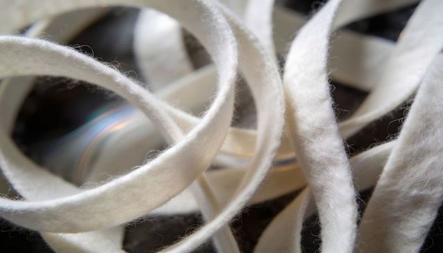 Curling white felt strips forming soft textured loops on dark reflective surface
