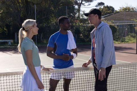 Tennis players and coach talking at net on outdoor court during sunny training session
