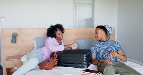 Young Couple Relaxing on Bed with Suitcase in Hotel Room