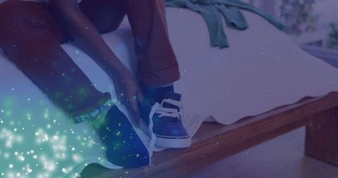 African american boy tying shoe laces at home with sparkle overlay