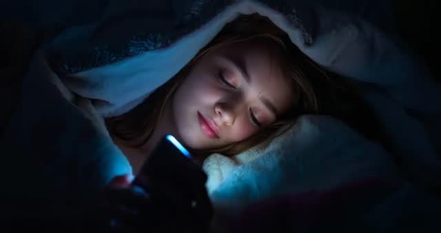 Teen Relaxing Under Blankets Using Smartphone at Night