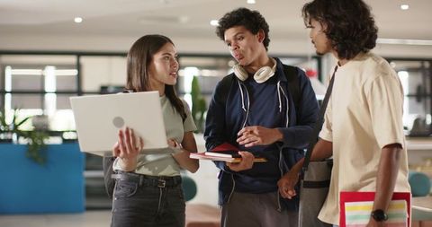 College students collaborating in modern campus lounge using laptop, notebooks, headphones