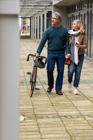 Senior couple walking with bicycle on urban walkway sharing coffee and conversation