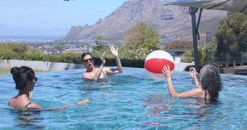 Mature women playing with red white beach ball in infinity pool with mountain view