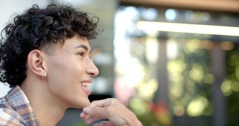 Young man smiling in profile while hand resting on chin at outdoor cafe patio with bokeh