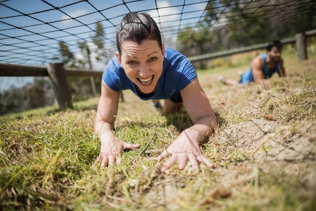 Fit woman crawling under the net during obstacle course in boot camp