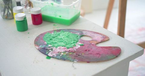 Wooden artist palette holding vibrant green acrylic paint with jars and brushes on studio table