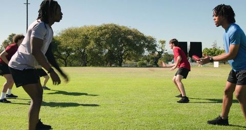 Multiracial young men practicing catch drill on sunny grass field building teamwork skills