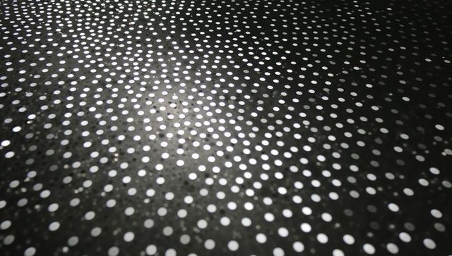 Monochrome perforated metal panel with reflective white dot grid and shallow depth