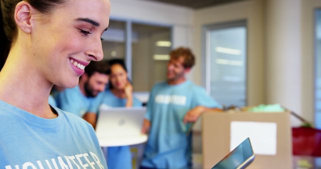 Smiling Female Volunteer Using Tablet with Team in Background - Download Free Stock Images Pikwizard.com