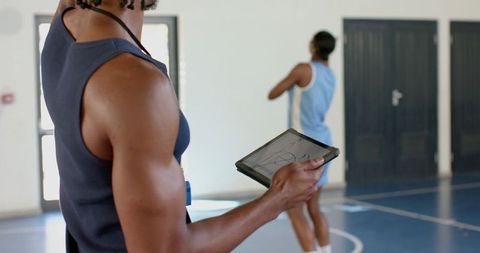 Coach guiding female basketball player with tablet on court
