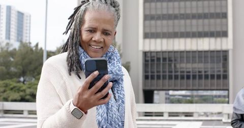 Senior African American woman checking smartphone on urban terrace wearing smartwatch
