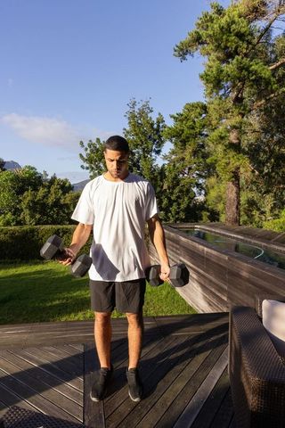 Hispanic man exercising outdoors with dumbbells near pool
