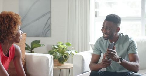 Smiling couple chatting with smartphone in bright modern living room, relaxed conversation