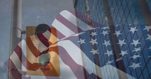 Waving us flag overlapping traffic light with green signal and glass office tower