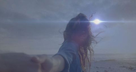 Woman Holding Hand on Ocean Shore with Sun Flare